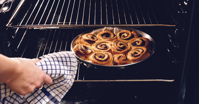 person taking cinnamon rolls out of oven
